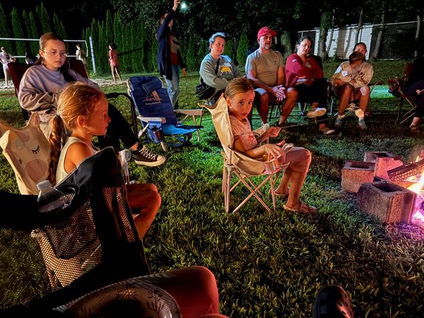 Kids and adults relaxing in camp chairs by the fire