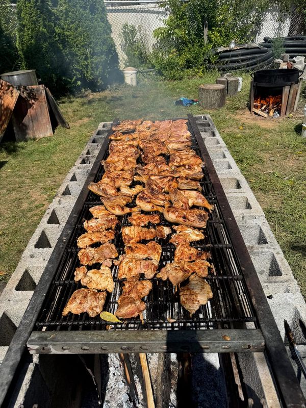 Rows of chicken cooking over an open-fire grill