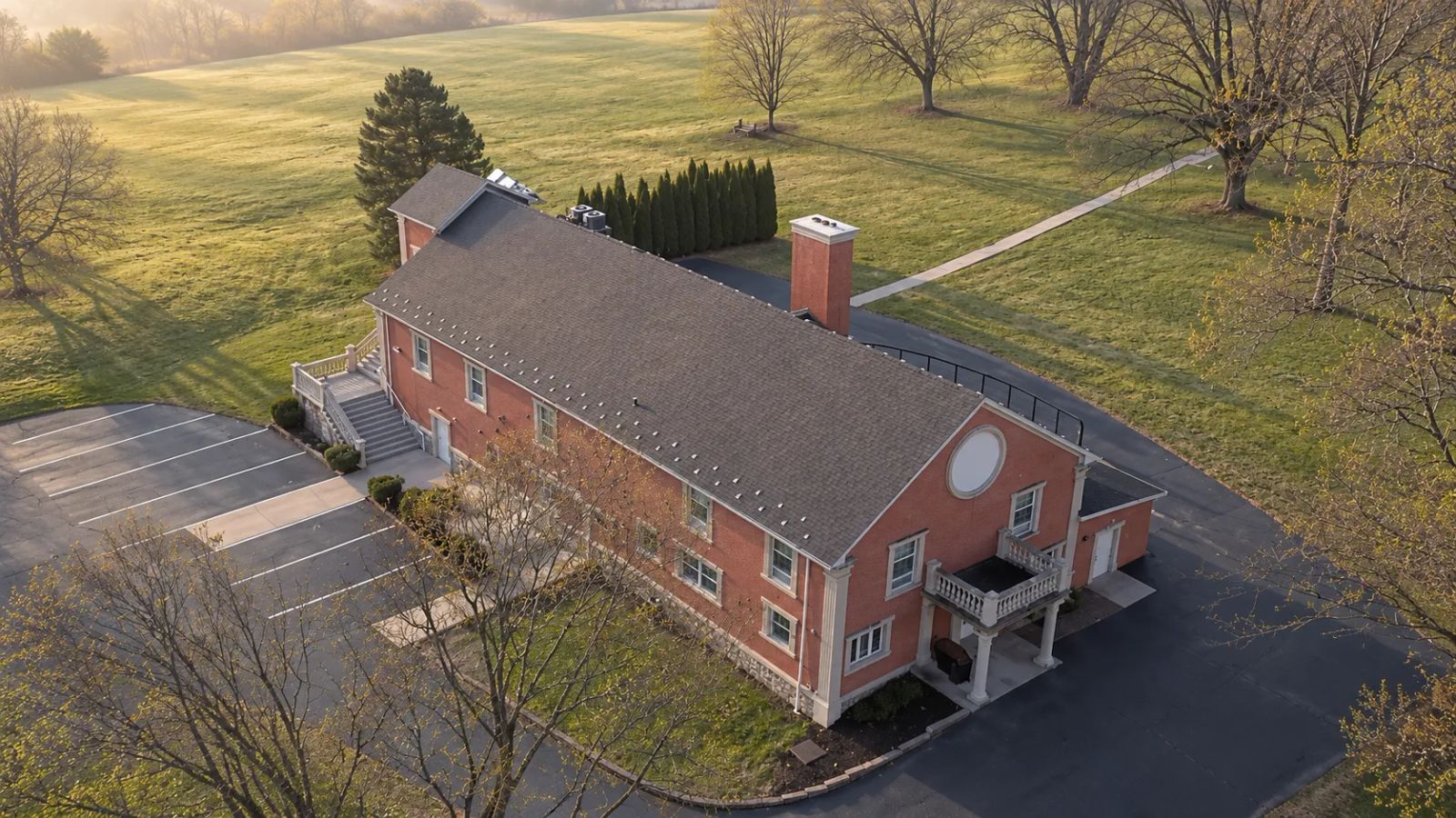 Aerial view of our red-brick church building surrounded by fields and trees in the morning light